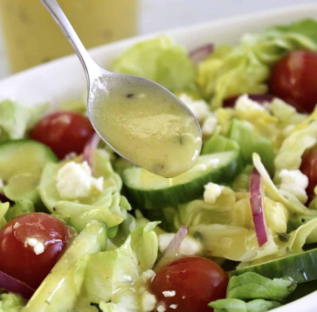 Lemon Vinaigrette being spooned over salad in white bowl