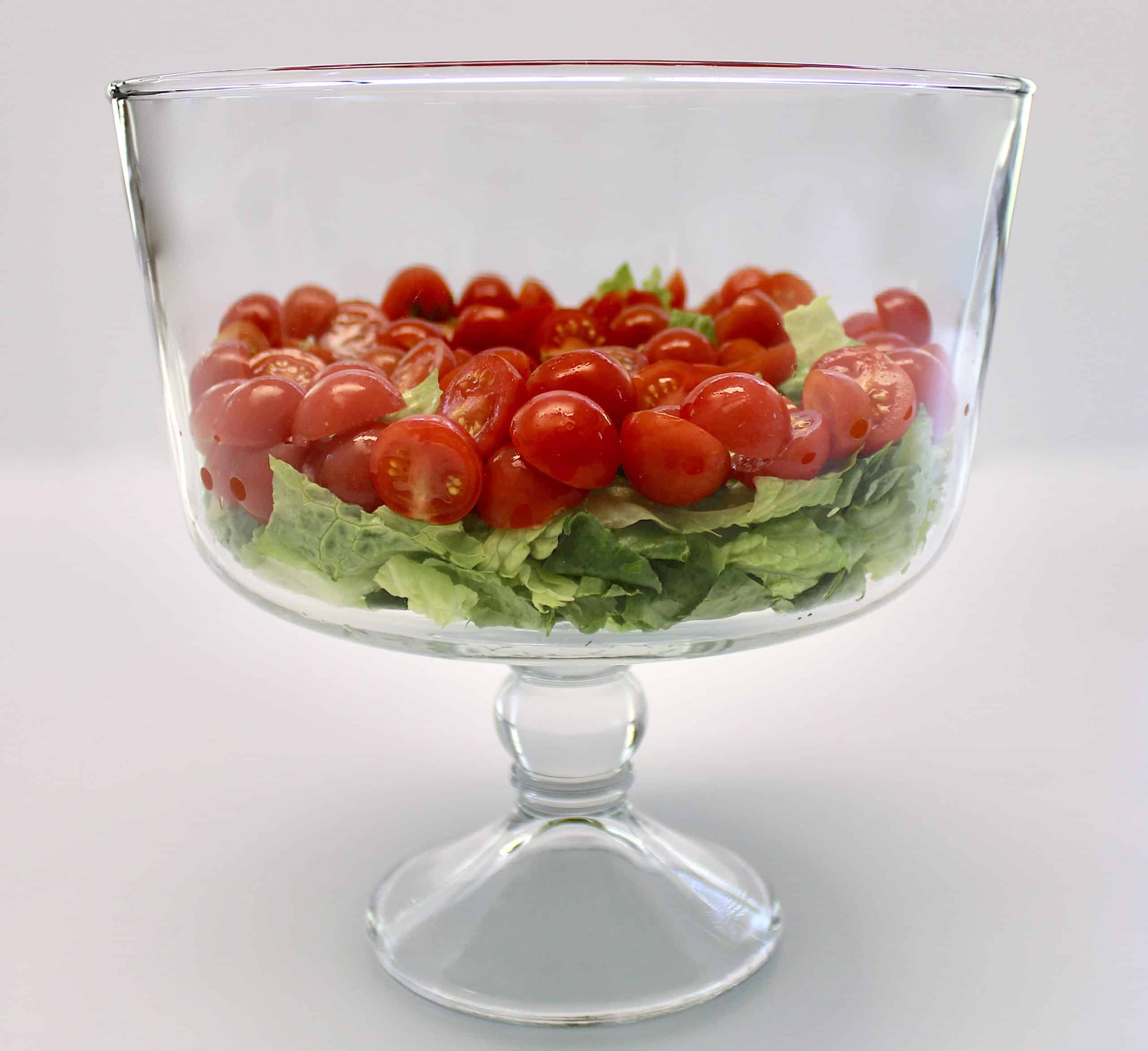 shredded lettuce and cut cherry tomatoes in glass trifle bowl