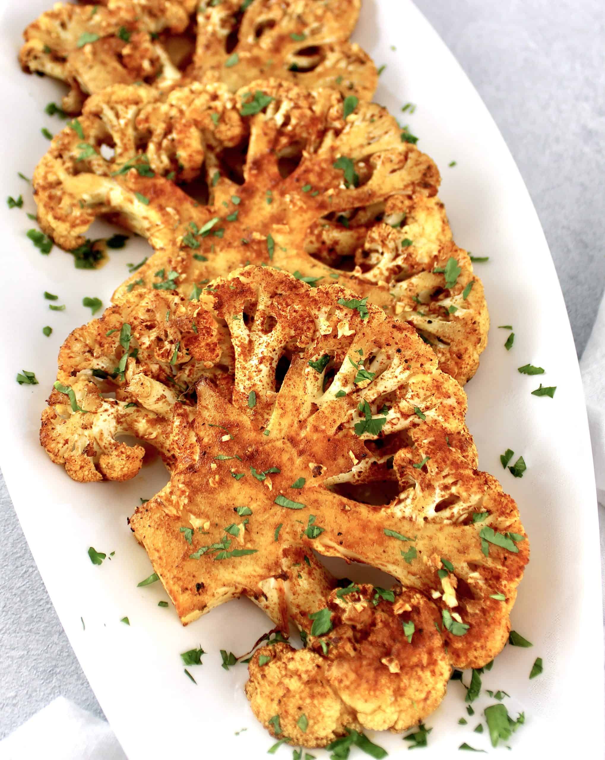 Roasted Cauliflower Steaks on white plate with chopped parsley on top