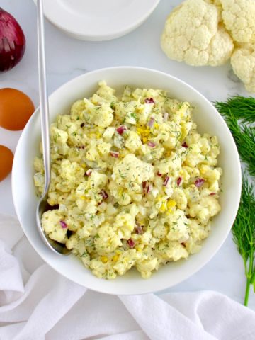 Cauliflower Potato Salad in white bowl with serving spoon